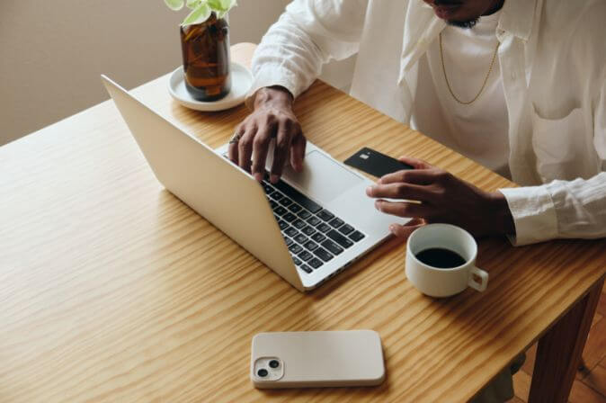 Black man sitting at a clean desk with his laptop, a beverage and a cup of coffee, learning about the guaranteed income