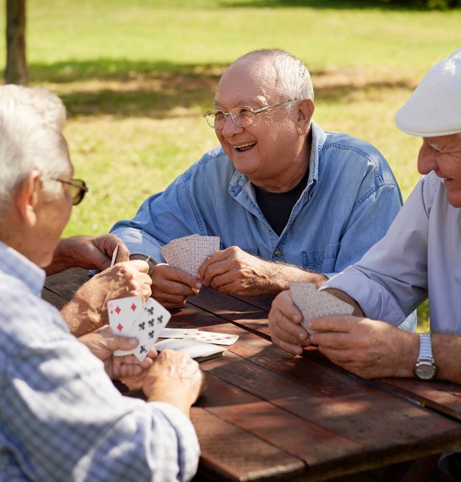 Four elderly men playing cards in the park, having fun, and discussing guaranteed income
