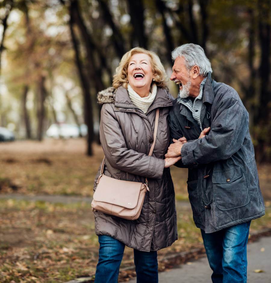 Senior couple laughing while on a walk in the park, discussing annuity income